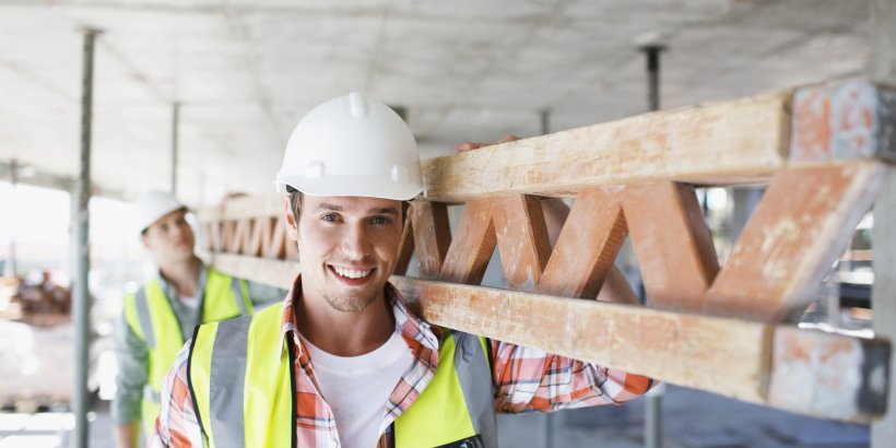 Männer in persönlichen Schutzausrüstung tragen Balken auf einer Baustelle